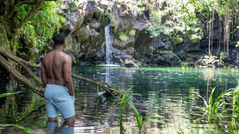 Ein Mann in einem Becken unter einem Wasserfall im Wald auf Mauritius