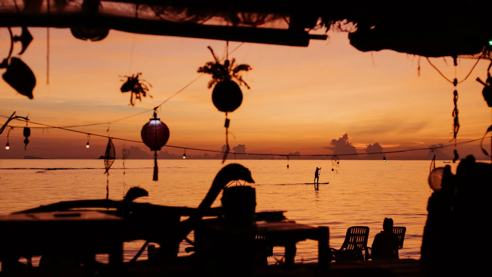 Laternen und Silhouetten einer Strandbar bei Sonnenuntergang