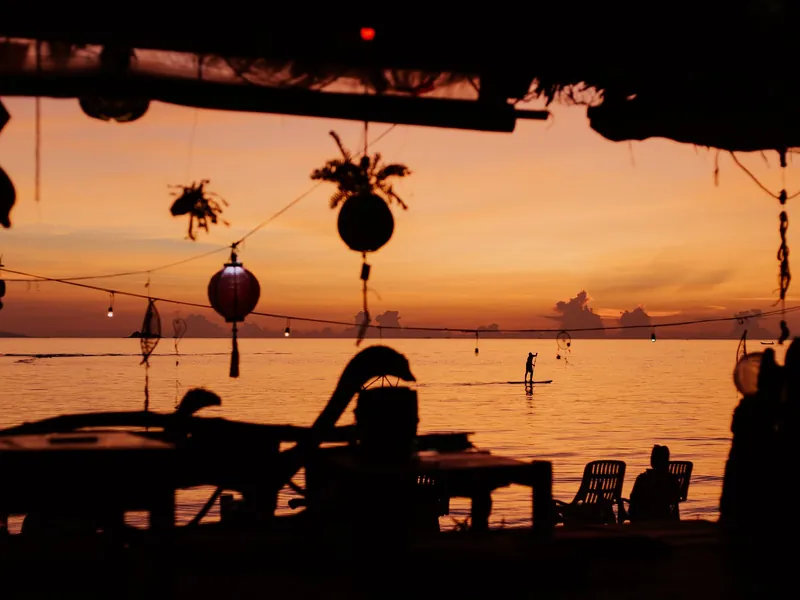 Laternen und Silhouetten einer Strandbar bei Sonnenuntergang
